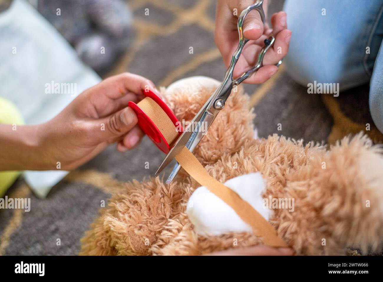 Hände schneiden während der Bastelzeit vorsichtig ein rotes Band an einem Teddybären ab Stockfoto