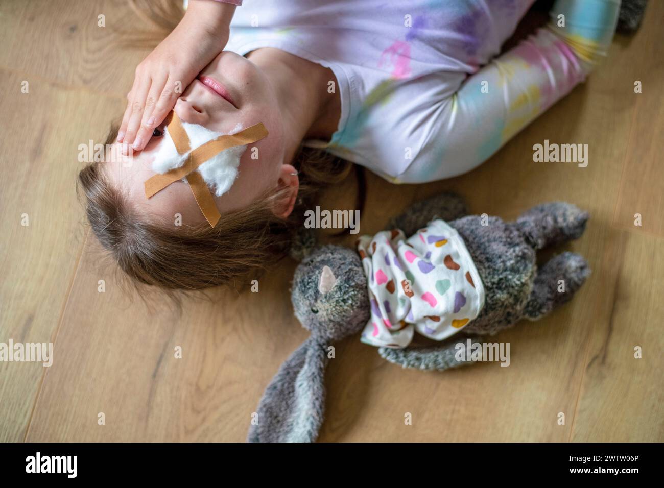 Ein junges Mädchen, das auf dem Boden liegt und mit ihrem Plüschhasen an ihrer Seite steht. Beide sehen so aus, als bräuchten sie ein paar Kleinigkeiten. Stockfoto