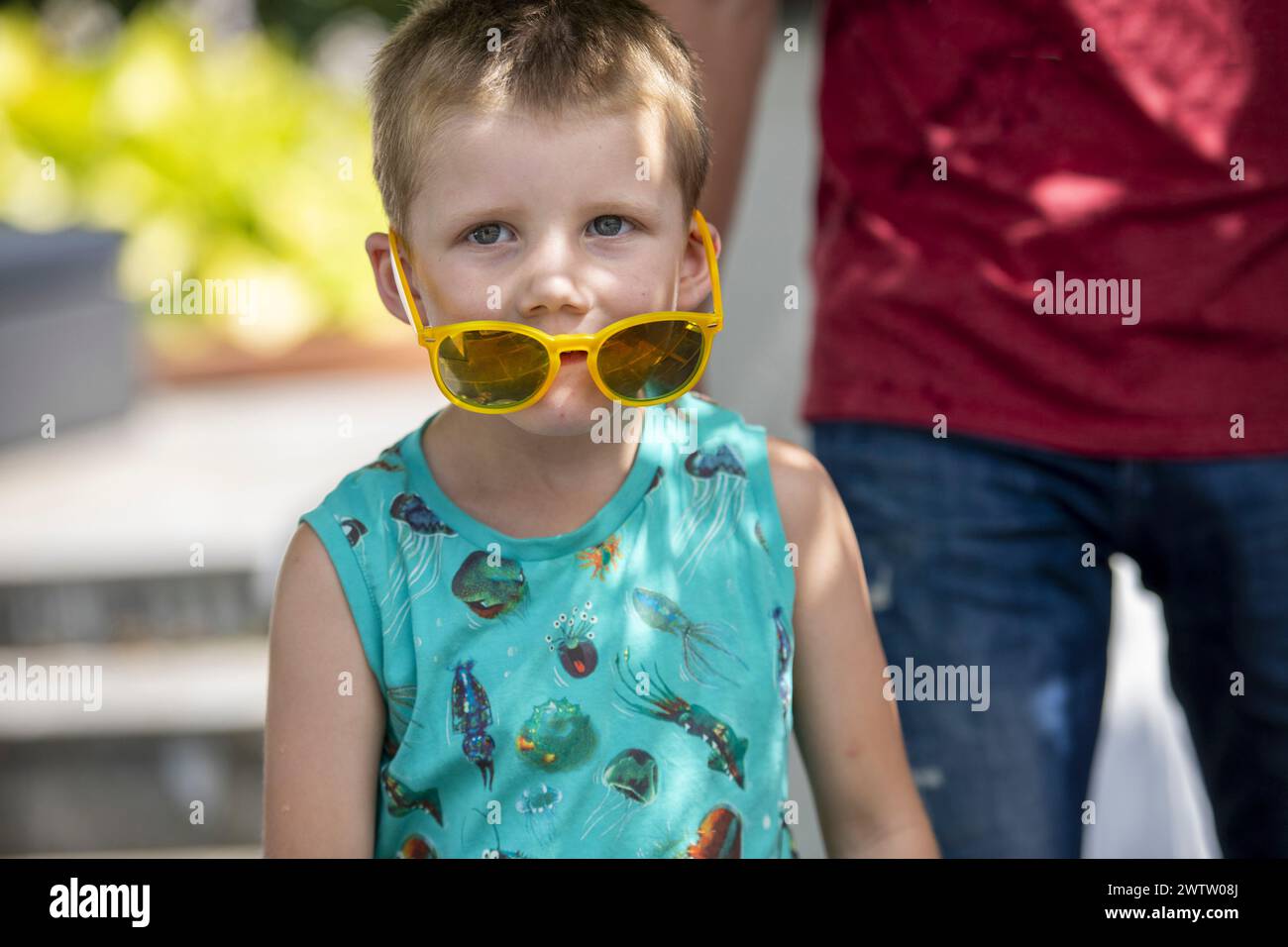 Kind in gelber Sonnenbrille und gemustertem Oberteil im Freien Stockfoto