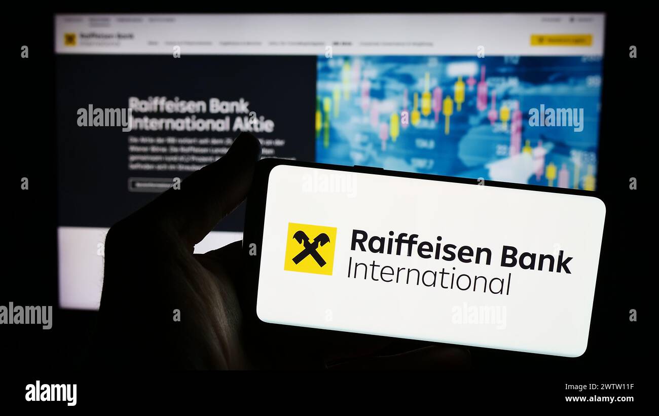 Person mit Smartphone und Logo der österreichischen Raiffeisen Bank International AG (RBI) vor der Website. Schwerpunkt auf dem Display des Telefons. Stockfoto