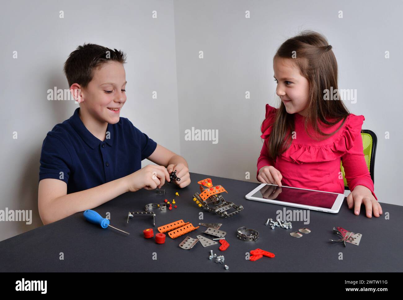 Mädchen und Jungen bauen Roboter mit Werkzeugen, programmieren mit Tablet. Bildungskonzept, Kreativität und Technologieforschung für Kinder Stockfoto