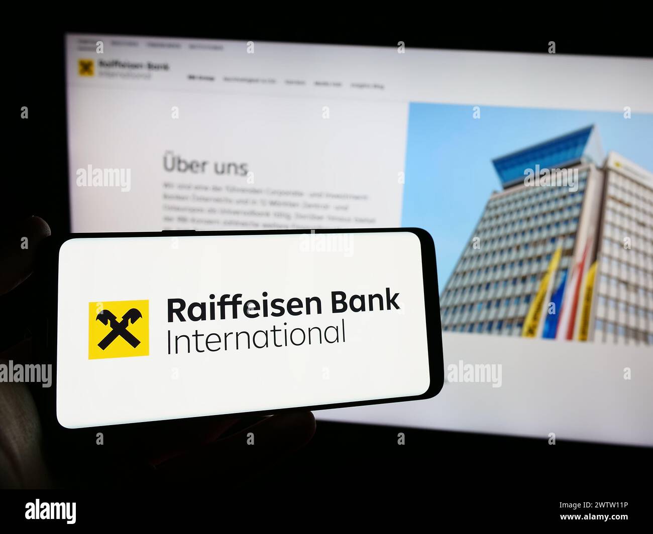 Person mit Mobiltelefon mit Logo der österreichischen Raiffeisen Bank International AG (RBI) vor der Webseite. Schwerpunkt auf dem Display des Telefons. Stockfoto