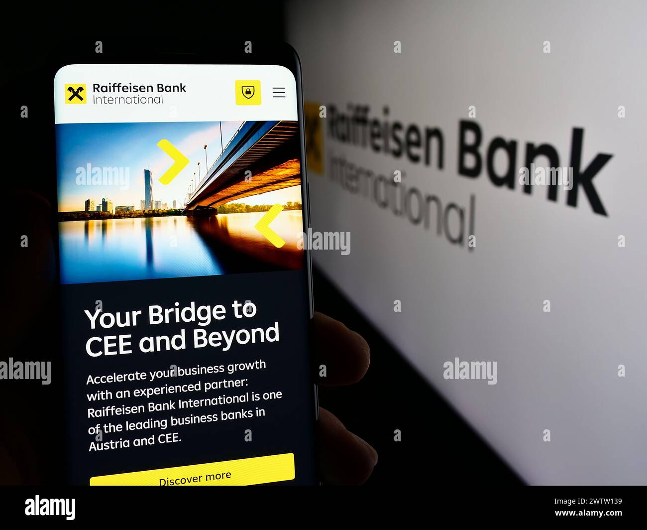 Person mit Smartphone mit Webseite der österreichischen Raiffeisen Bank International AG (RBI) mit Logo. Konzentrieren Sie sich auf die Mitte des Telefondisplays. Stockfoto