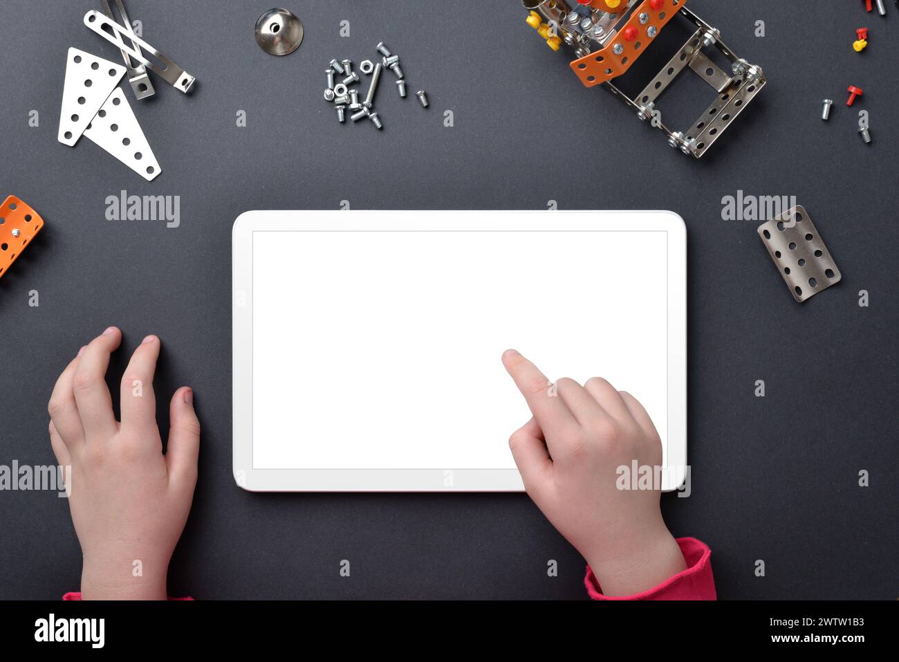 Tablet-Mockup auf dem Schreibtisch. Kinderhände berühren isoliertes Display. Draufsicht, flache Schreibtischkomposition mit kleinen Metallteilen und Schrauben Stockfoto