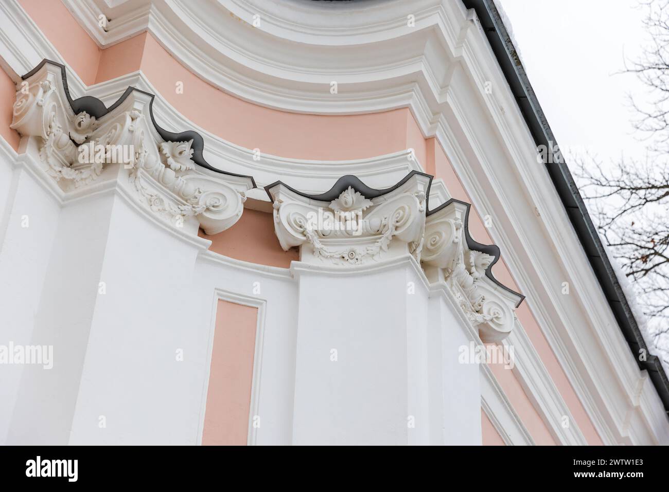 Klassischer Portikus mit rosa und weißen Details unter hellem Himmel. Säulen und Ecken Stockfoto
