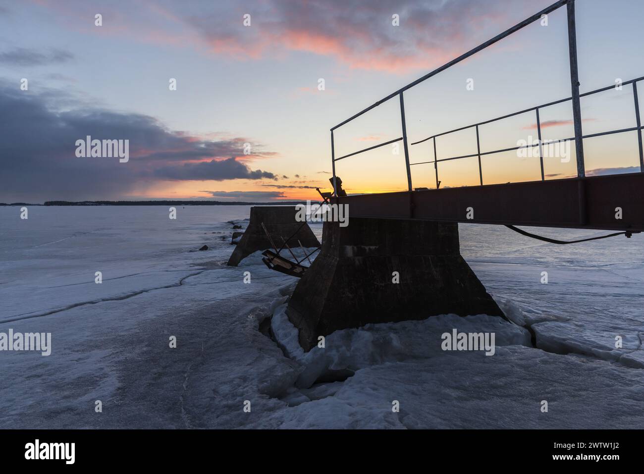 Verlassener, kaputter Pier liegt an einem Winterabend unter Sonnenuntergang Stockfoto