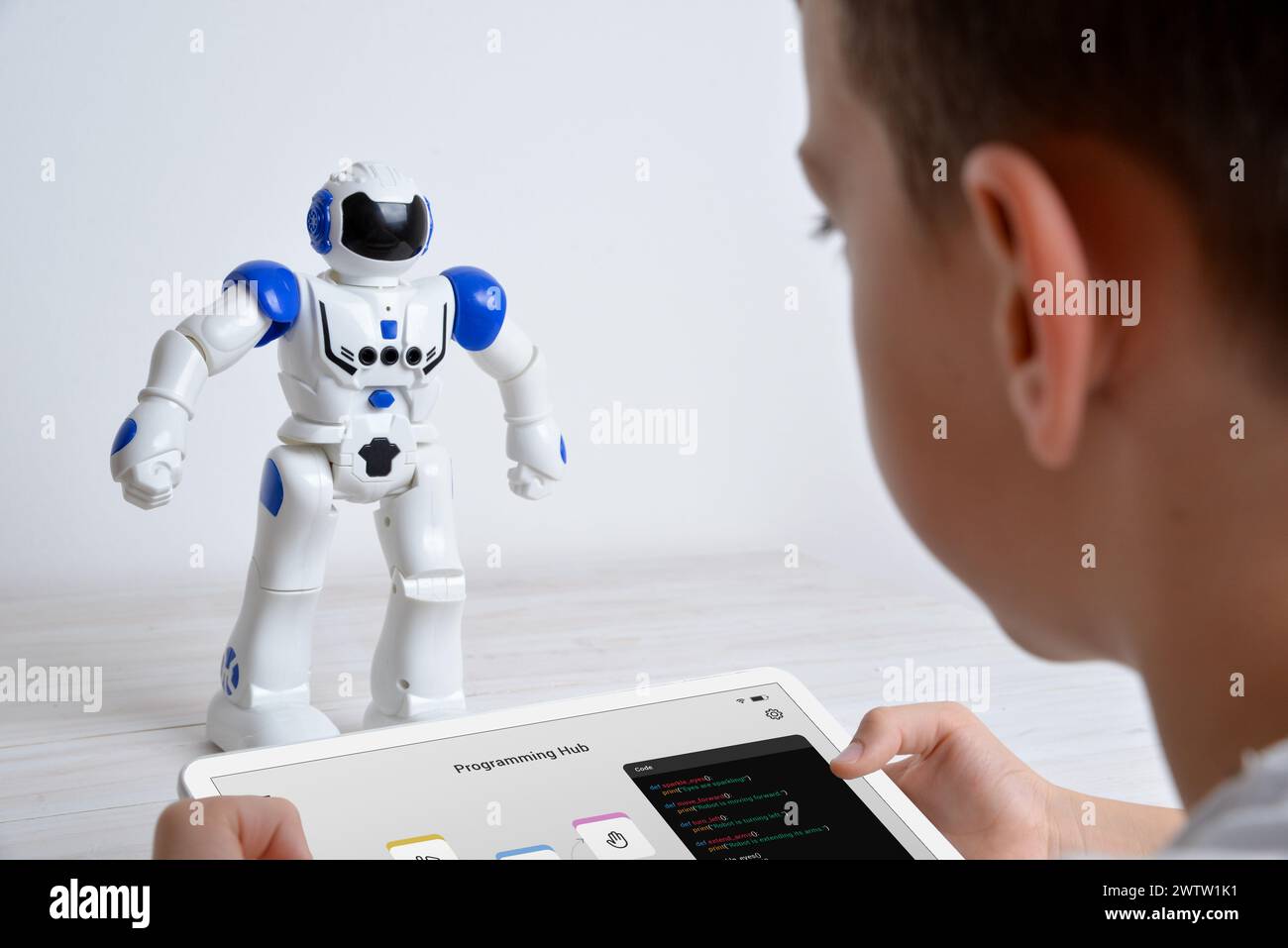 Boy steuert den Roboter mit einem Tablet auf dem Schreibtisch. Darstellung von Bildung, Technologie, Innovation und interaktiven Lernerlebnissen in Robotik und Programmen Stockfoto
