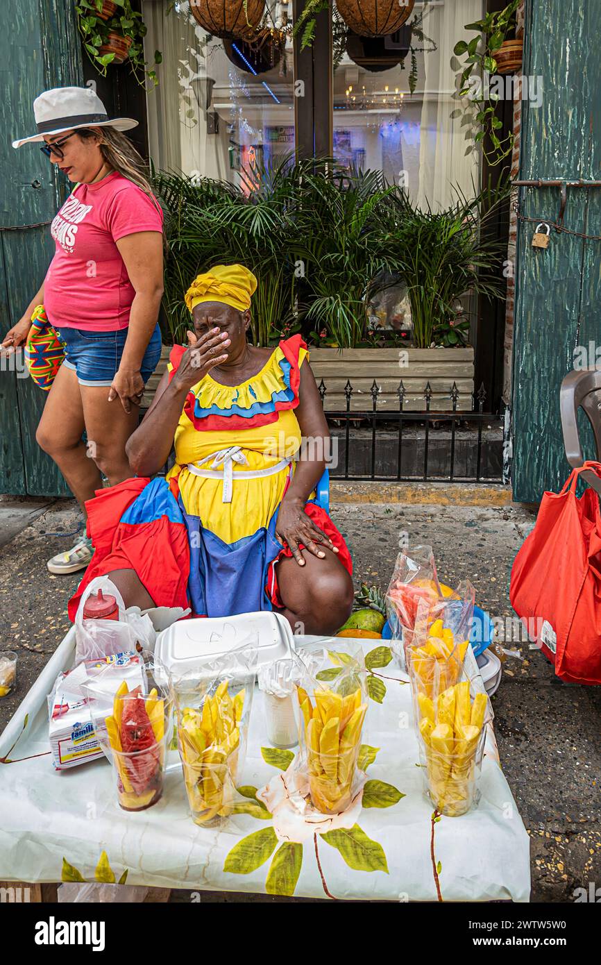 Cartagena, Kolumbien - 25. Juli 2023: Nahaufnahme: Weibliche Straßenverkäuferin in farbenfroher traditioneller Kleidung verkauft Süßigkeiten von kleinen Tischen. Pedest Stockfoto