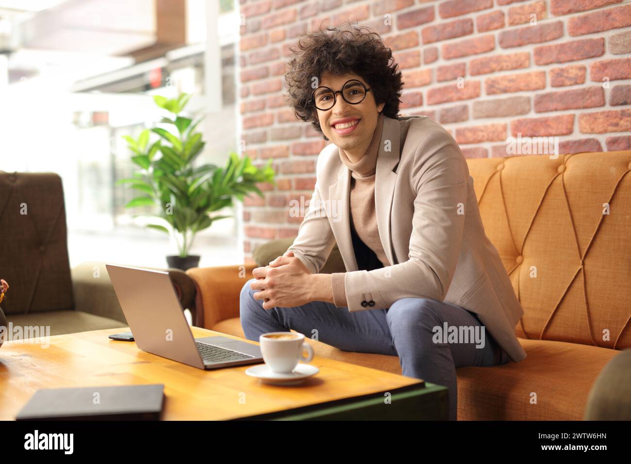 Ein lächelnder junger Mann in einem Café, der einen Kaffee trinkt und an einem Laptop arbeitet Stockfoto