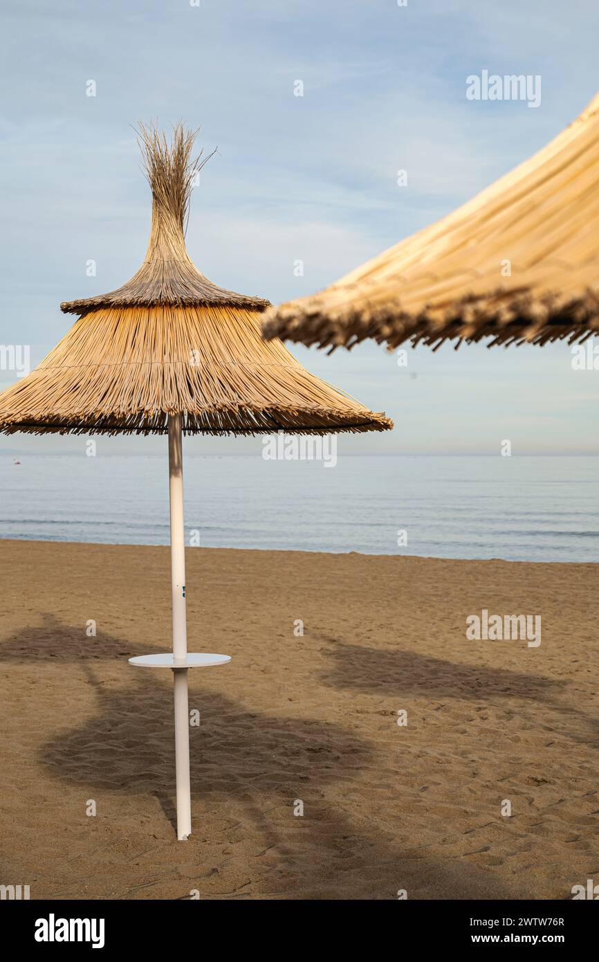 Strohschirm im Vordergrund an einem Strand bei Sonnenuntergang, ruhige und ruhige Umgebung ohne Menschen. Stockfoto