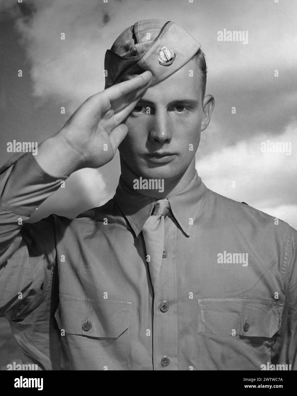 Junger Militärmann in Hemd und Krawatte mit Mütze, starrend geradeaus, grüßt mit einer Hand, die aufmerksam ist Stockfoto