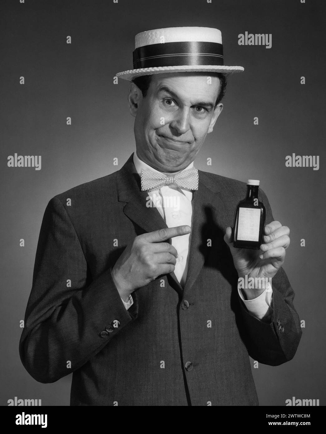 Porträt eines Mannes in Strohhut-Anzug und Bowtie, der eine Flasche Medizin in der einen Hand hält, während die andere Hand auf die Flasche zeigt, während er sein Verkaufsgespräch gibt Stockfoto