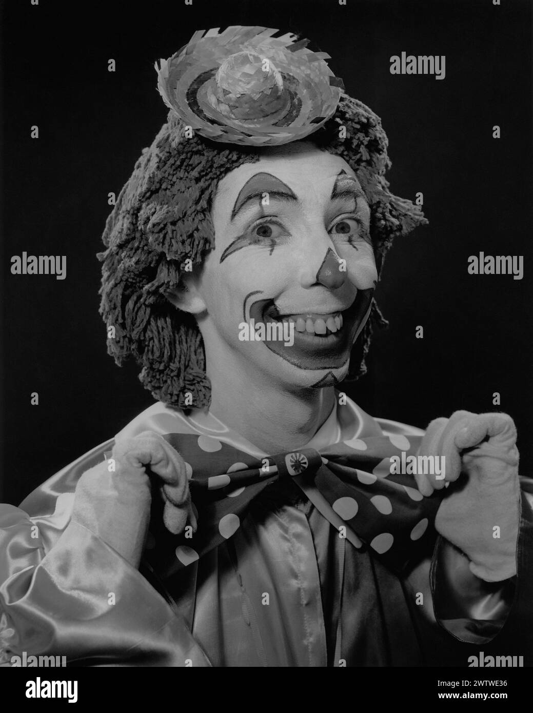 Nahaufnahme eines Mannes in einem Clown-Outfit, Gesicht bemalt, große Bowtie, Moppkopf und einen Mini-Strohhut auf dem Kopf Stockfoto