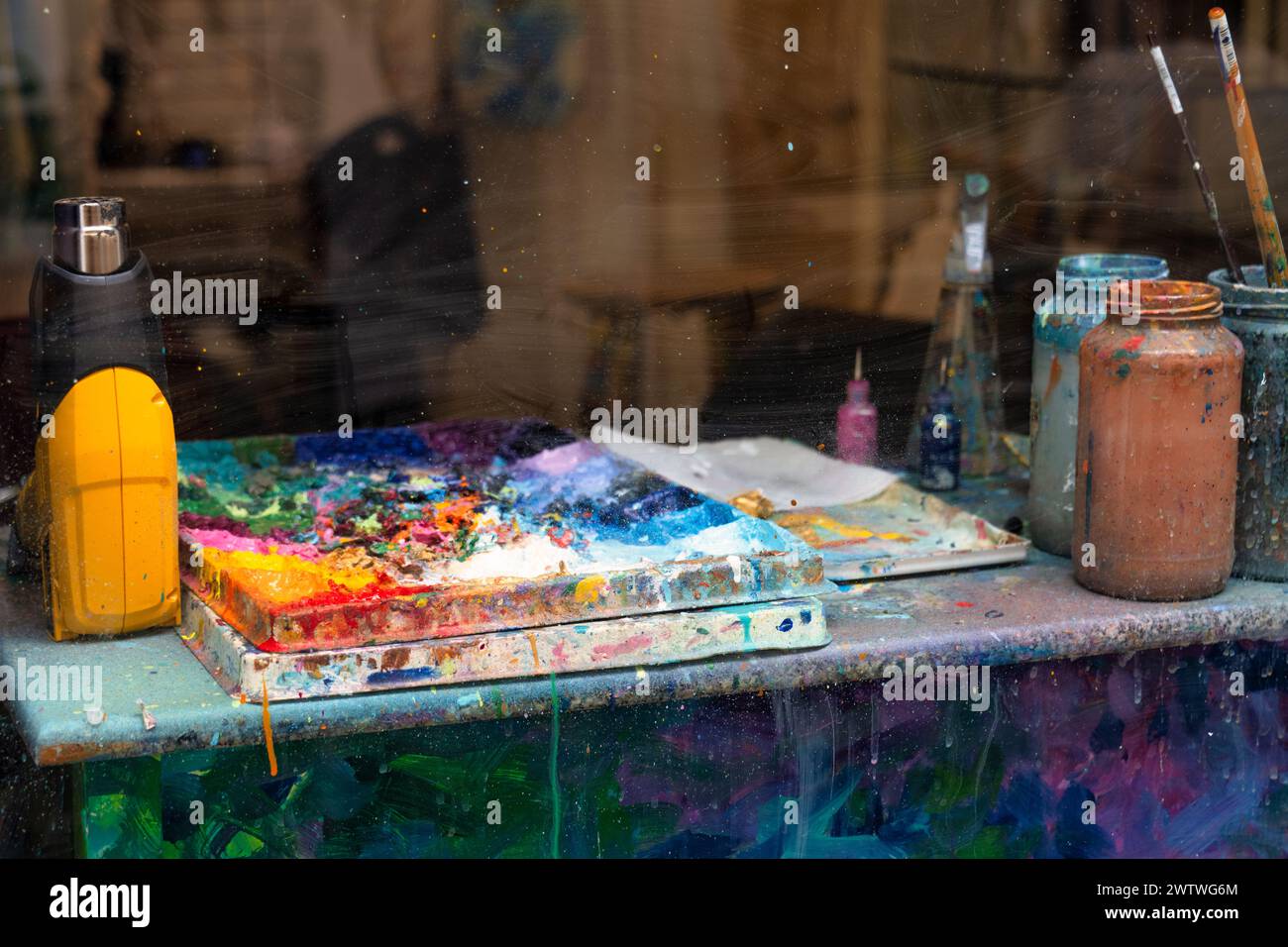 Ein Blick aus der Nähe auf den Arbeitsbereich eines Künstlers mit einer unordentlichen Farbpalette und fleckigen Gläsern, die mit Pinseln gefüllt sind Stockfoto