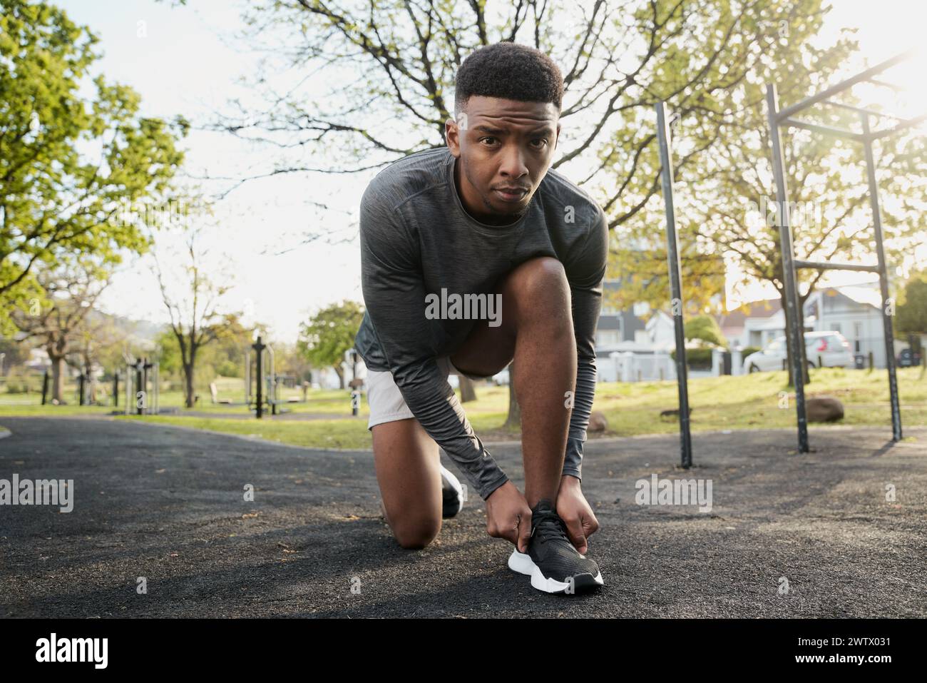 Junger schwarzer Mann in Sportkleidung, der in die Kamera schaut, während er kniet und Schnürsenkel im Park bindet Stockfoto