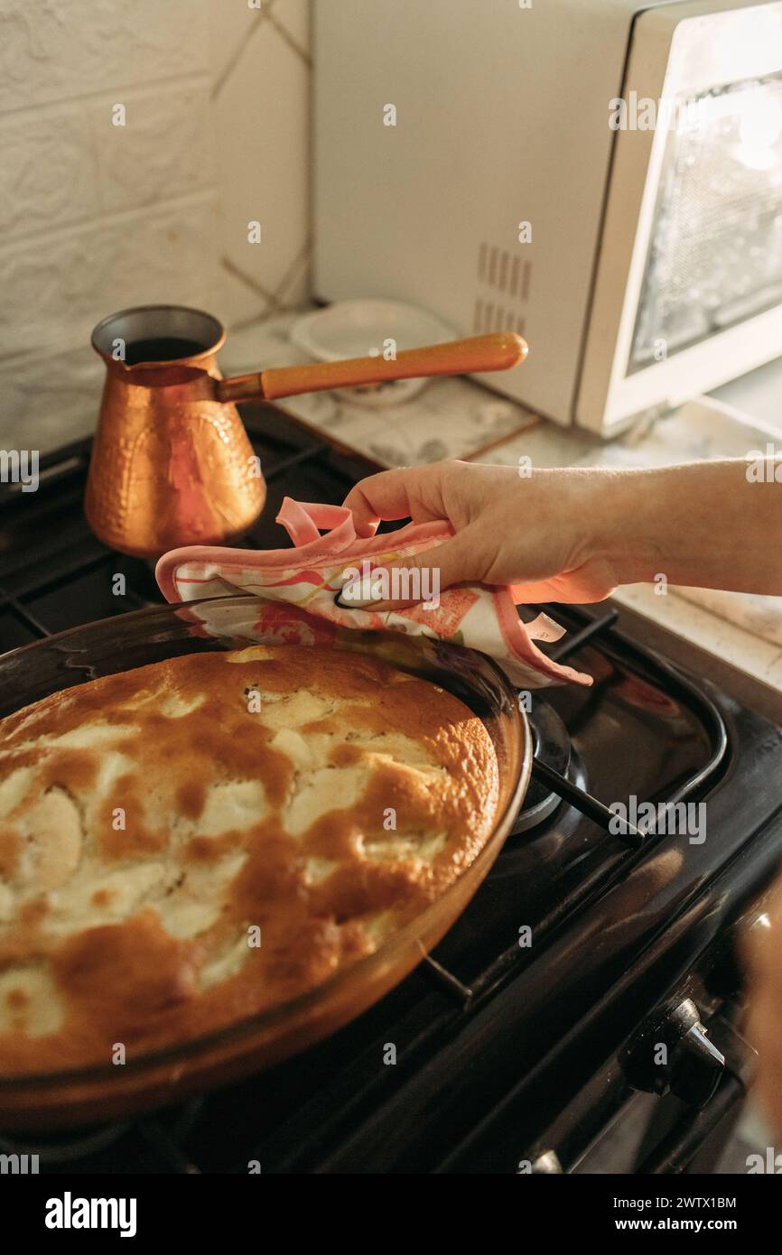 Eine Person mit Ofenhandschuhen, die einen rohen Kuchen zum Backen in einen vorgewärmten Ofen einfügt. Stockfoto