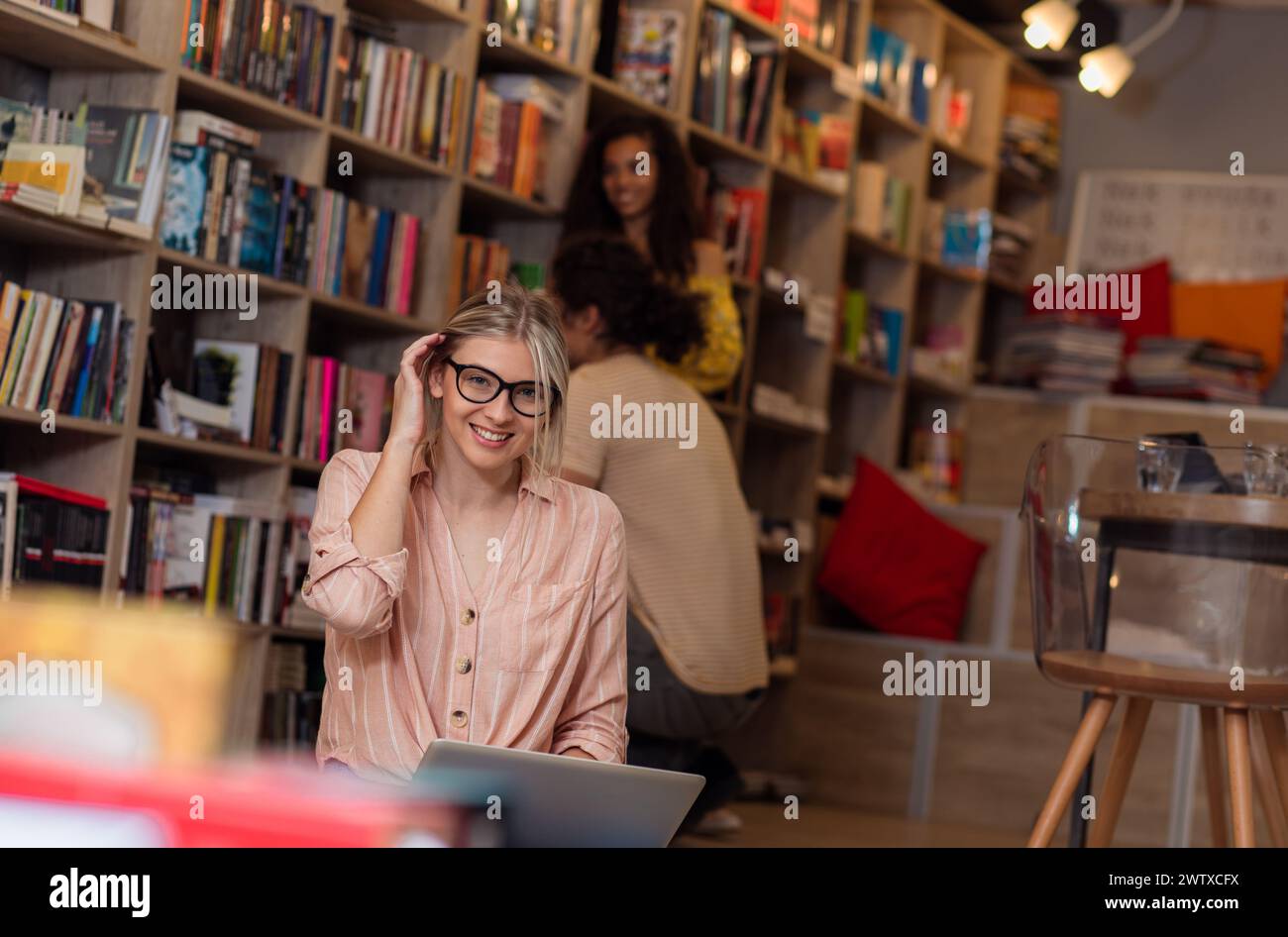 Porträt einer jungen Studentin, die mit ihren Freunden im Hintergrund in der Bibliothek sitzt. Stockfoto