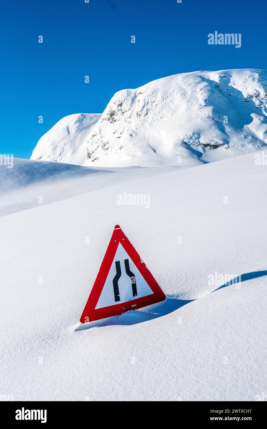 Straßenschild, das aus tiefem Schnee auf einer unter Schnee vergrabenen Straße in Norwegen ragt Stockfoto
