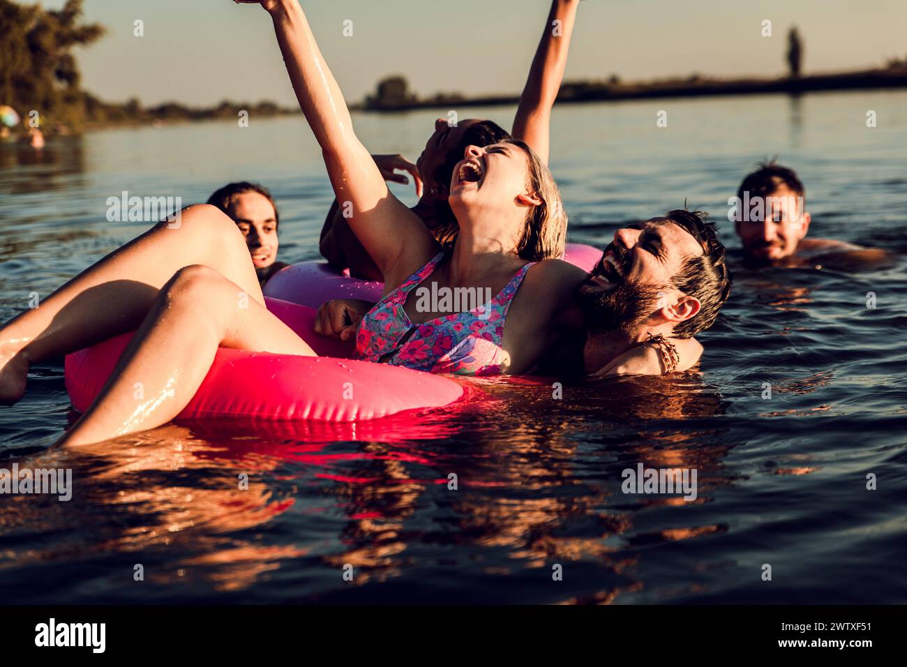 Gruppe von jungen Freunden, die Spaß haben und einen Sommertag beim Schwimmen am See genießen. Stockfoto