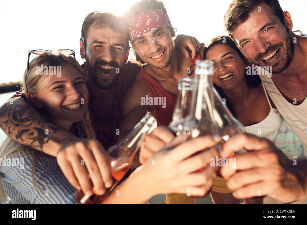 Porträt von Freunden, die auf einem Pier stehen und mit alkoholischem Getränk anstoßen und einen Sommertag am See genießen. Stockfoto