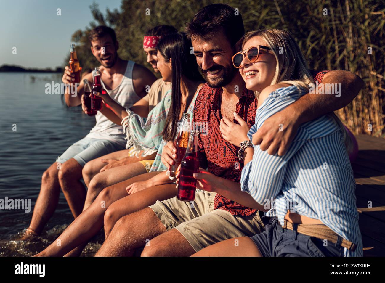 Eine Gruppe von Freunden sitzt am Rande eines Piers, hat Spaß und genießt einen Sommertag am See. Stockfoto