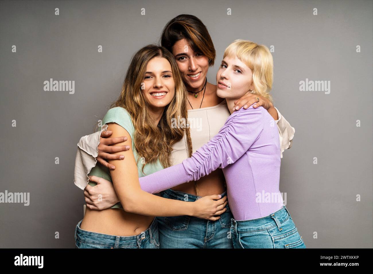Gruppe von drei jungen Frauen - umarmen - multirassische Freundinnen, die lächeln, sich verbinden und umarmen - Vielfalt und Zusammengehörigkeit vertreten; Stockfoto