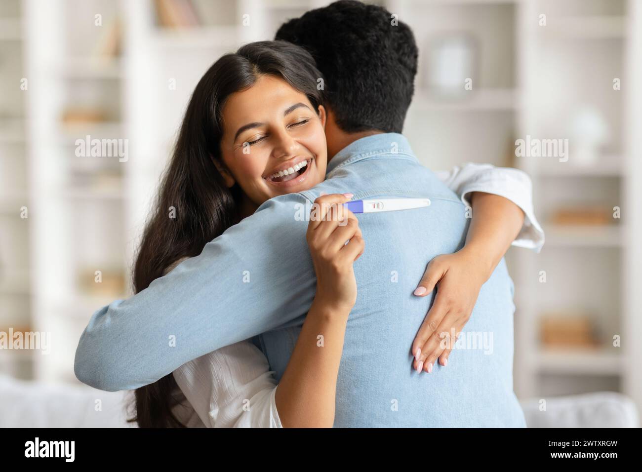 Indische Frau umarmt Mann mit positivem Schwangerschaftstest Stockfoto