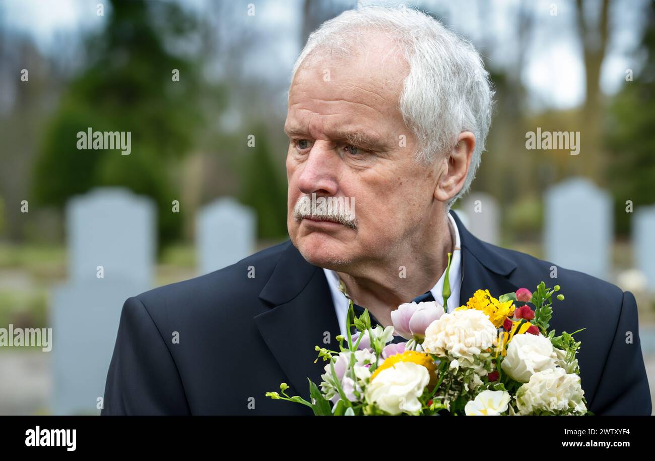 Trauriger alter Mann mit Blumen, der auf dem Friedhof trauert. Stockfoto