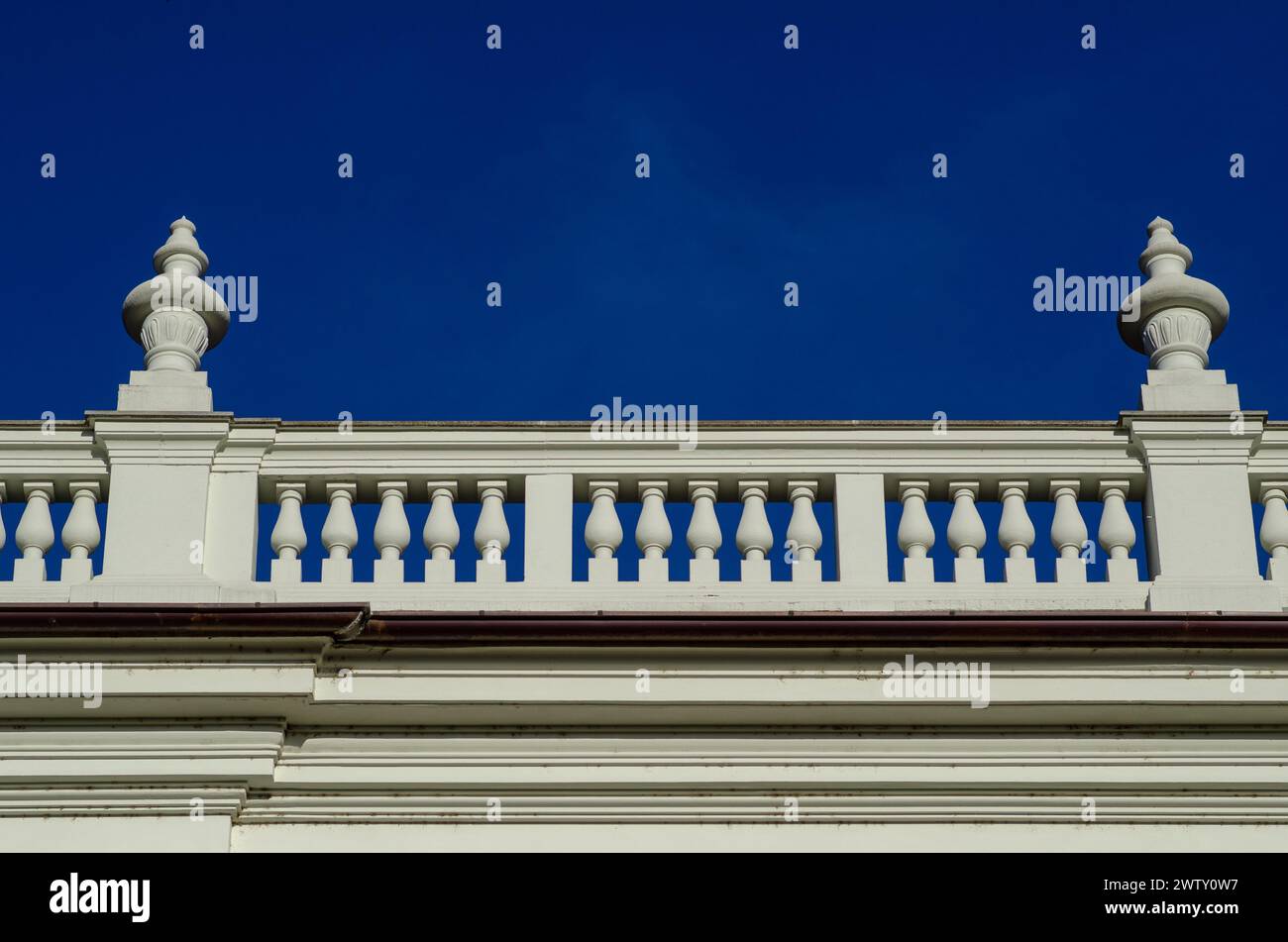 Detail eines eleganten edlen Palastes mit neoklassizistischen Elementen der Balustrade auf dem Kegel mit Säulen an der Fassade. Hintergrund der intensive blaue Himmel. Stockfoto