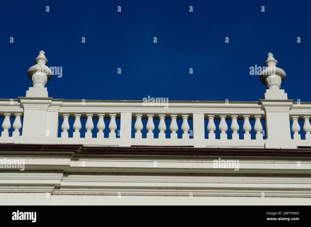 Detail eines eleganten edlen Palastes mit neoklassizistischen Elementen der Balustrade auf dem Kegel mit Säulen an der Fassade. Hintergrund der intensive blaue Himmel. Stockfoto