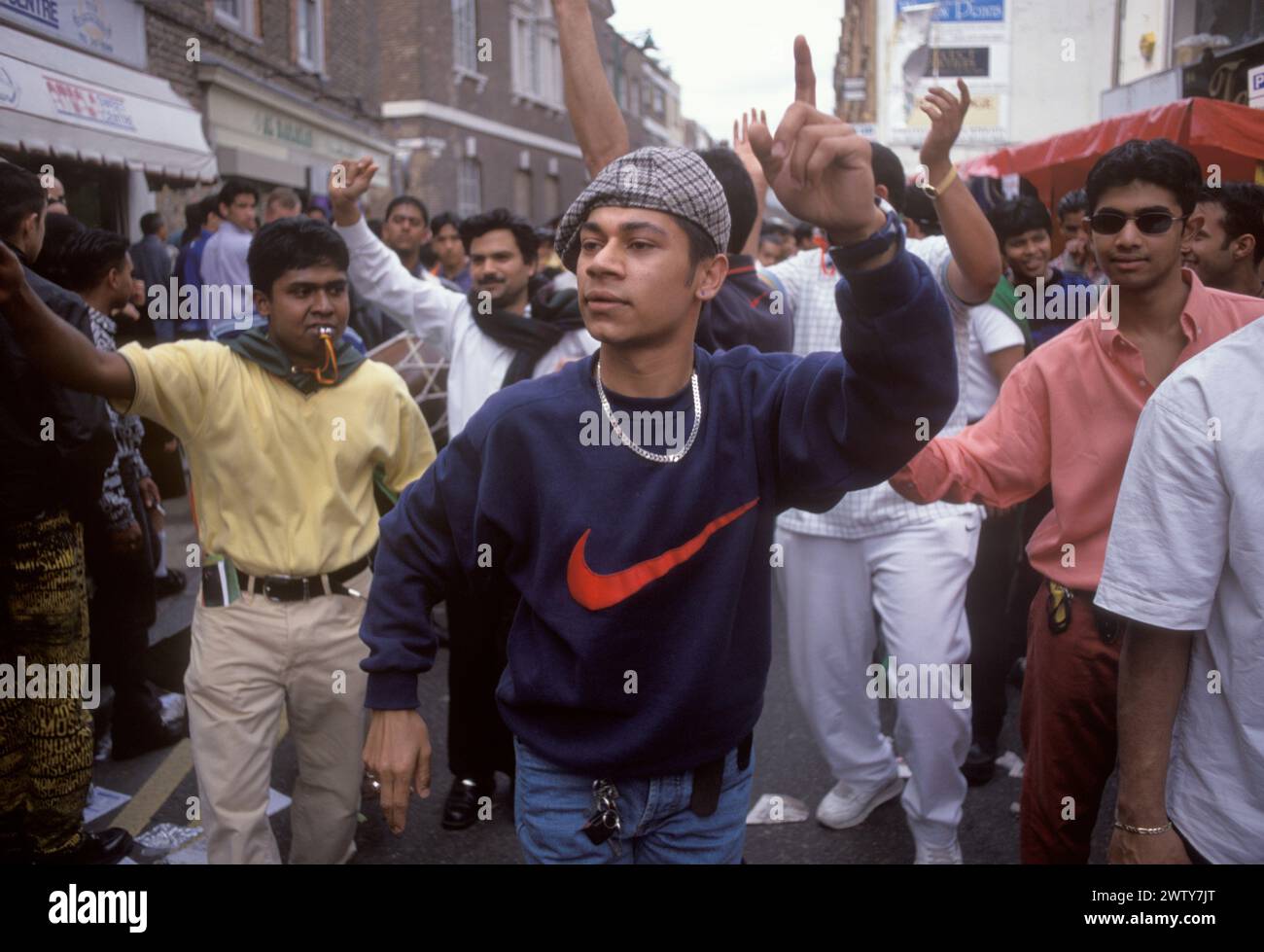 Die muslimische Gemeinde Bangladeschs in Brick Lane Whitechapel feiert das islamische Neujahr, auch Hijri-Neujahr genannt. Bangladesch Teenager Jungen tanzen durch die Straße. Einer trägt ein Sweatshirt mit einem riesigen roten „Häkchen“ das Nike Logo – Swoosh Logo. Juli 1999 1990: UK HOMER SYKES Stockfoto