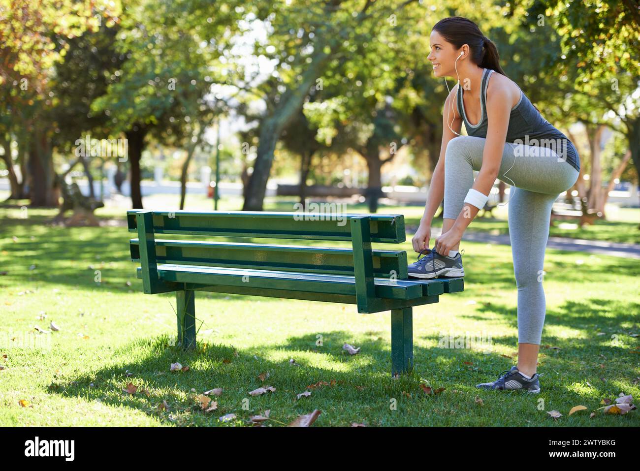 Glückliche Frau, Läufer oder Schnürsenkel im Freien, Kopfhörer oder Audio-Streaming für Sport in der Natur. Lady, Lächeln oder Musik für Wellness beim Joggen Stockfoto