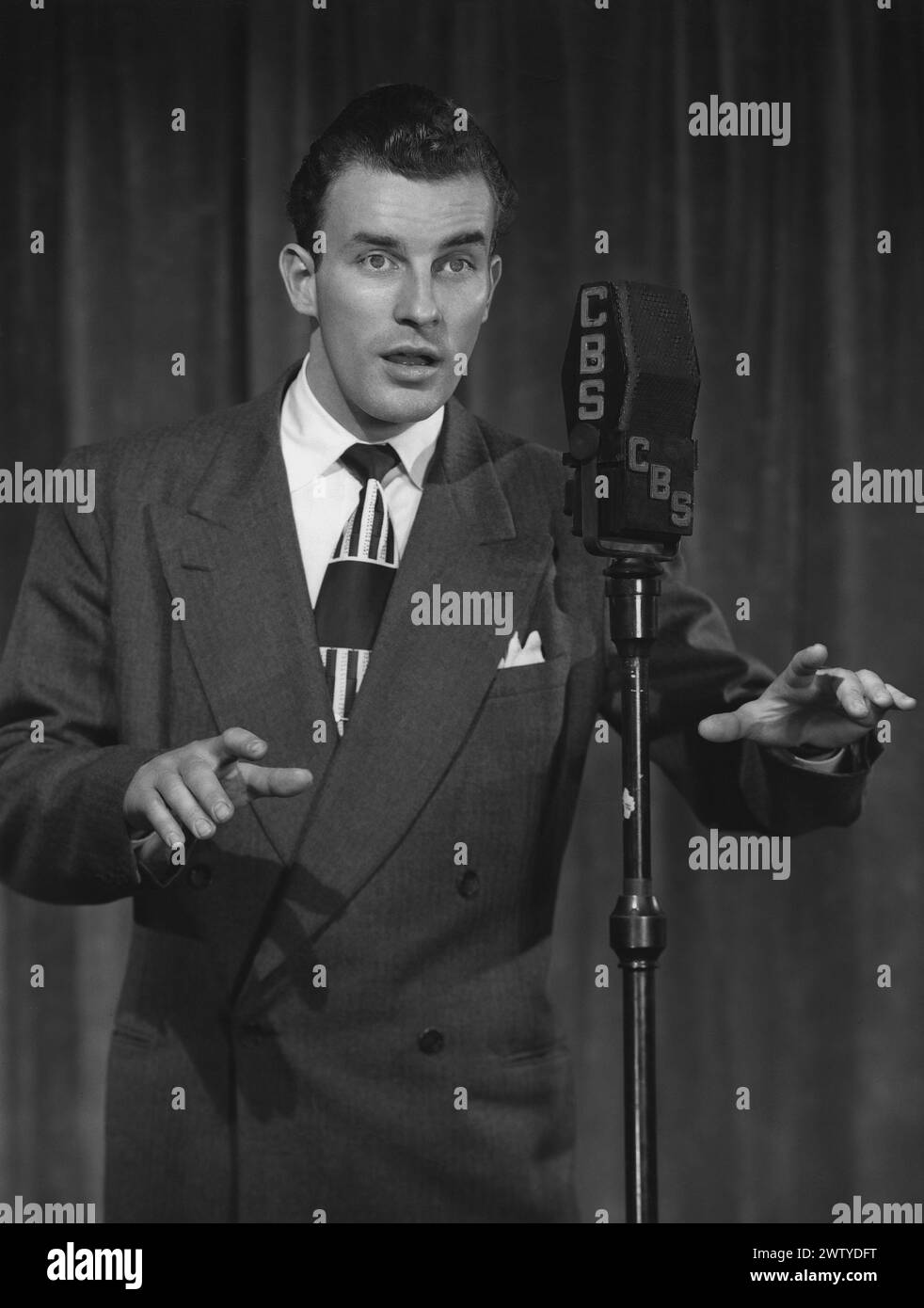 Junger Mann in einem Anzug, der in einem Studio vor einem CBS-Mikrofon aufsteht und den Audioteil der Show macht Stockfoto