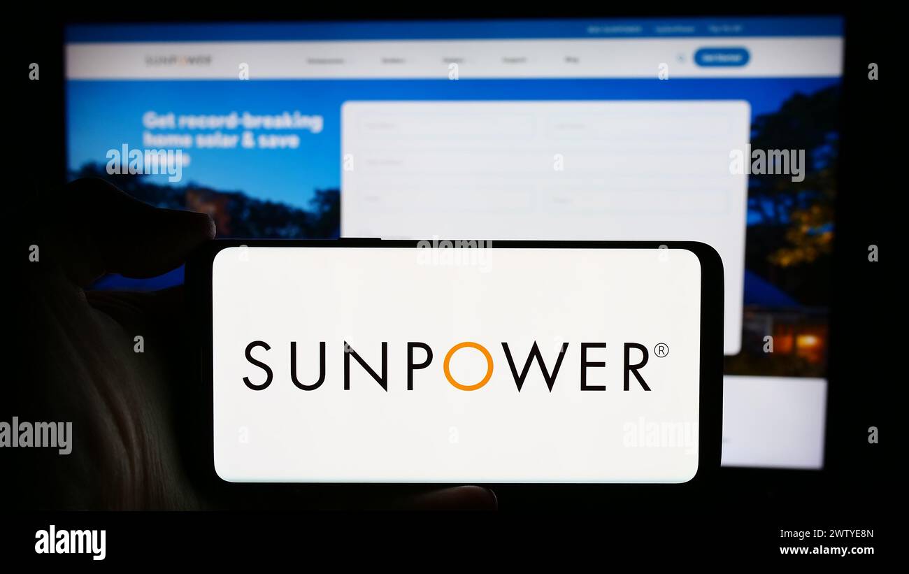Person, die ein Mobiltelefon mit dem Logo des US-amerikanischen Photovoltaik-Unternehmens SunPower Corporation vor der Webseite hält. Schwerpunkt auf dem Display des Telefons. Stockfoto