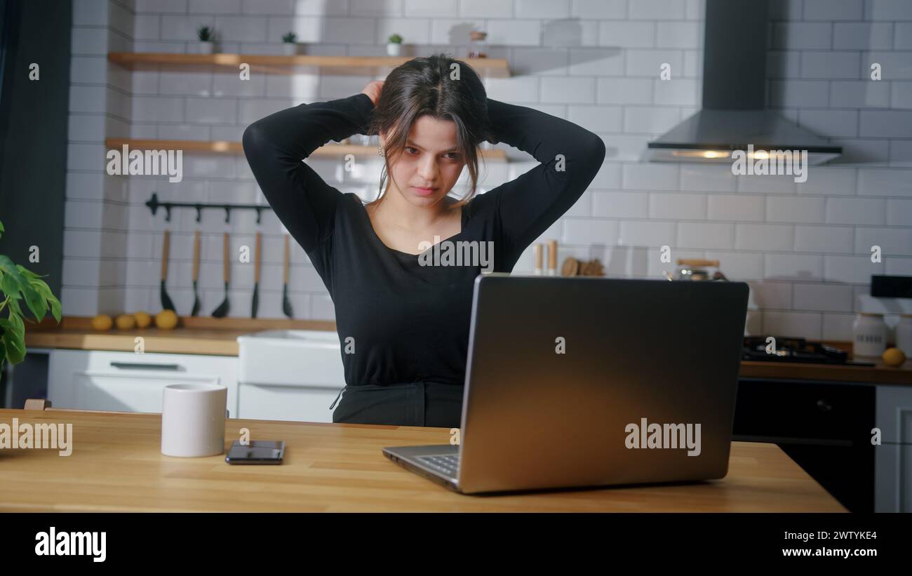 Junge Frau, die in der Küche sitzt und E-Mails auf dem Laptop liest, Nachricht lesen, gute Nachrichten erhalten oder Lotterie gewinnen feiert großartige Gelegenheit fühlt sich glücklich Stockfoto