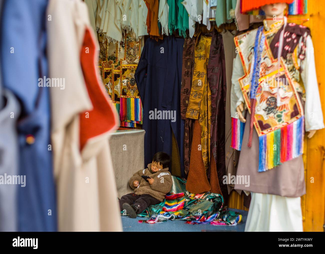 Junger asiatischer Junge, der auf dem Kleidermarkt sitzt Stockfoto