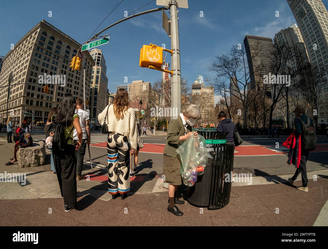 Frau sammelt Dosen und Flaschen neben Fußgängern, darunter eine mit Hose der Marke Zara am Donnerstag, den 14. März 2024, in Flatiron in New York. (© Richard B. Levine) Stockfoto