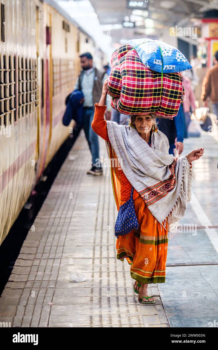 Eine ältere Indianerin, die Güter auf dem Kopf an einem Bahnhof trägt Stockfoto