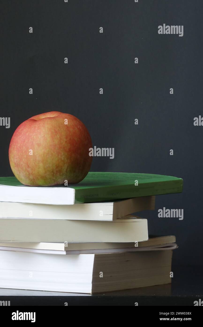 Ein leuchtender roter Apfel, der auf einem Stapel Bücher ruht Stockfoto