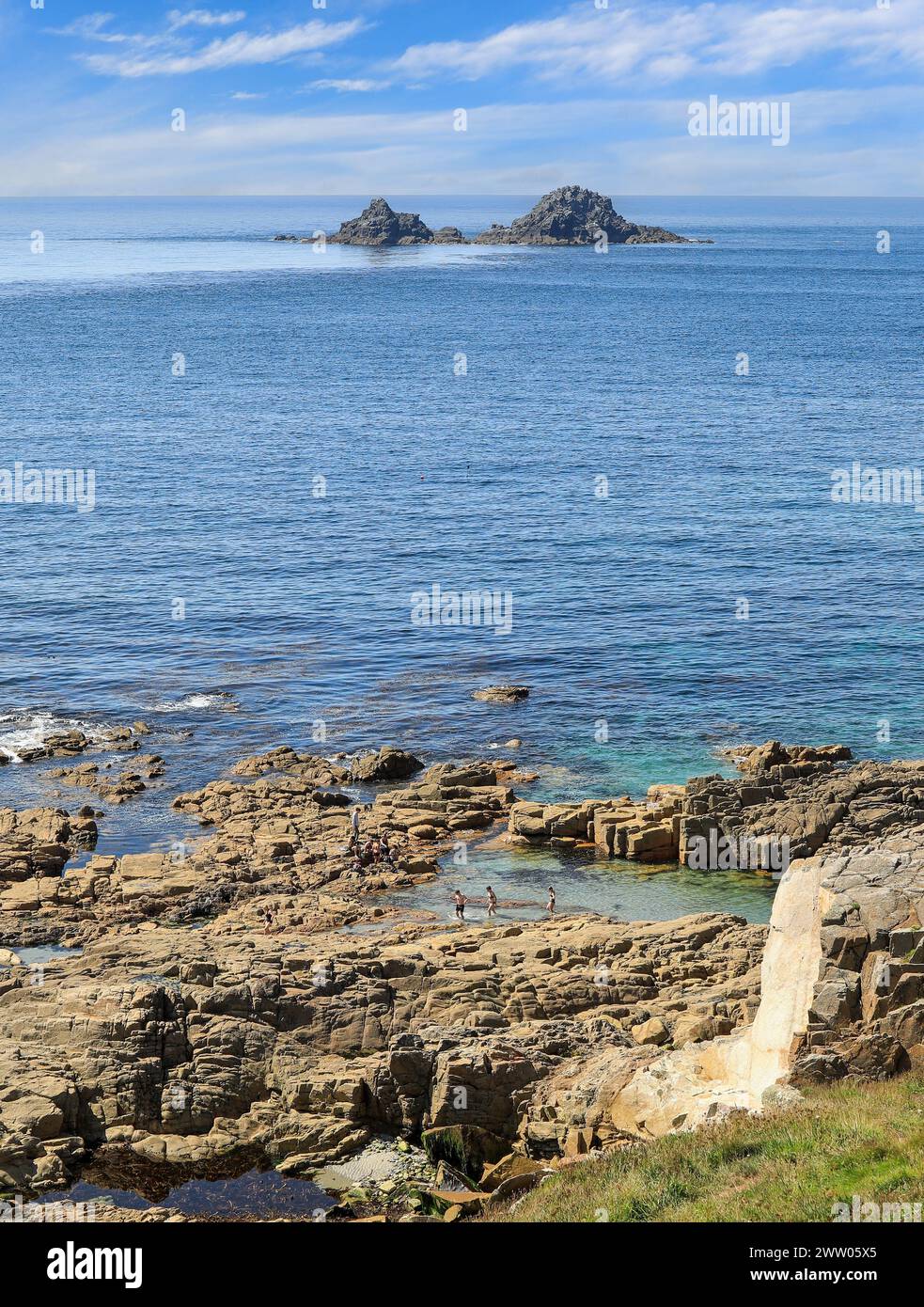 Menschen schwimmen und sonnen auf den Felsen, mit den Brisons Felsen in der Nähe von Cape Cornwall, St Just, Cornwall, West Country, England, UK Stockfoto