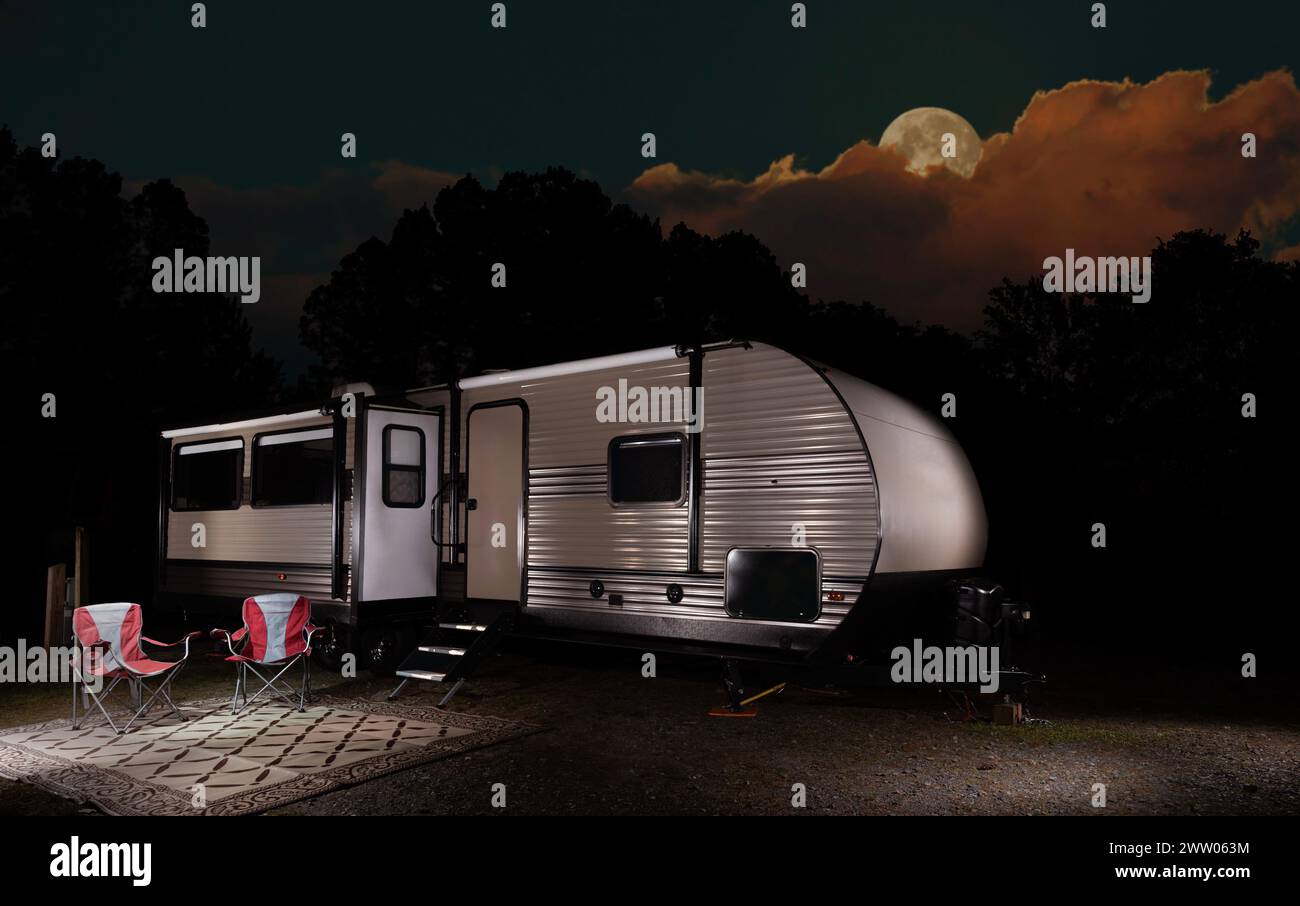 Orange und Gelb leuchten auf dem Mond tief über einem Wald hinter einem Campingplatz in abgelegener Lage. Stockfoto