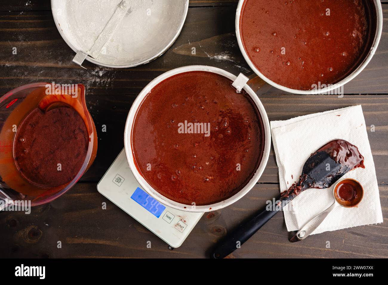 Wiegekuchenpfannen gefüllt mit Schokoladenteig: Runde bemehlte Kuchenpfannen, die mit einer digitalen Küchenwaage gewogen werden, um eine gleichmäßige Verteilung und Größe zu gewährleisten Stockfoto