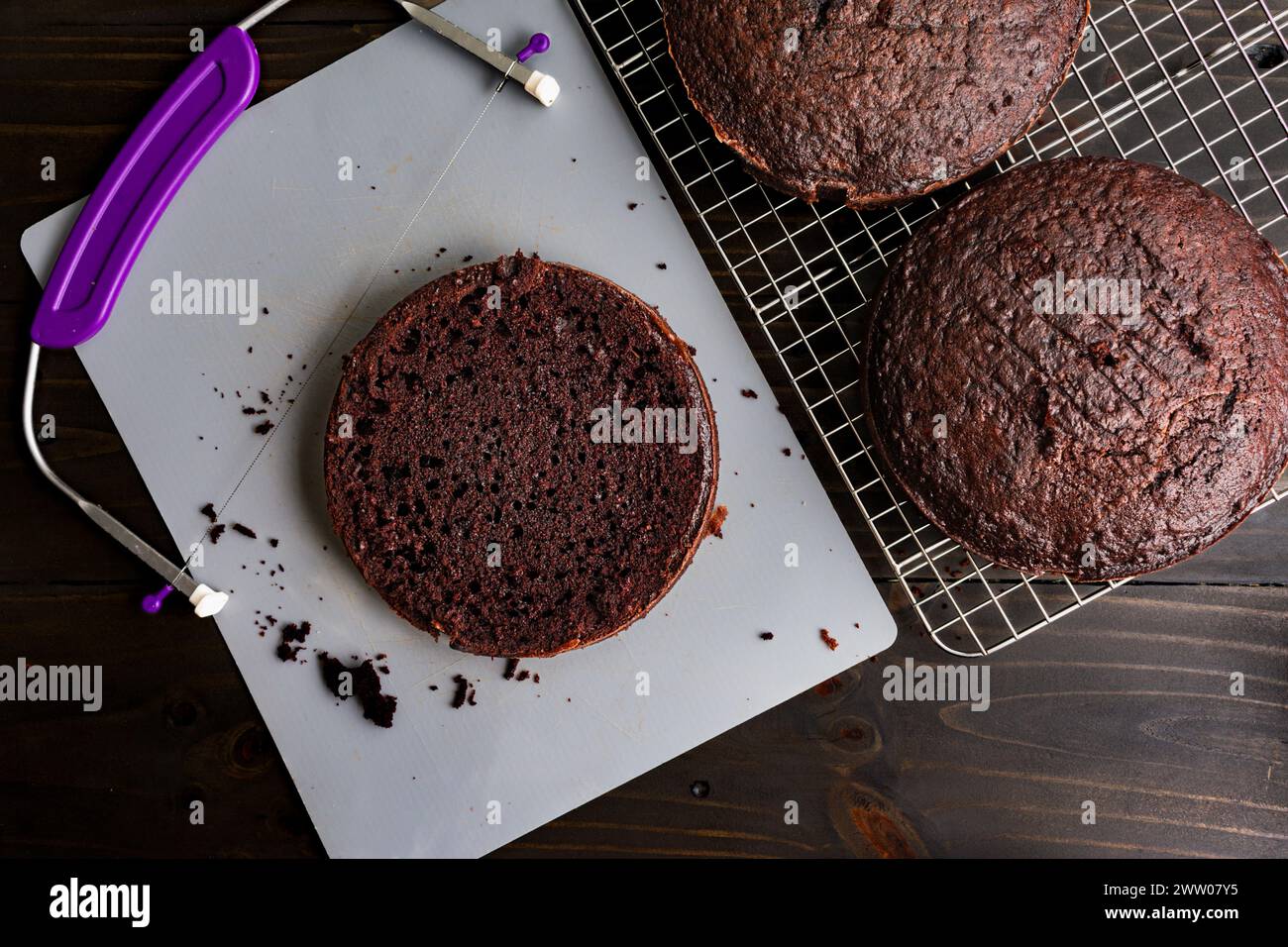 Runden Schokoladenkuchen auf eine gleichmäßige Höhe ausrichten: Runde dunkle Schokoladenkuchen werden nach dem Abkühlen auf einem Drahtgestell mit einem Drahtkuchennivelliergerät nivelliert Stockfoto