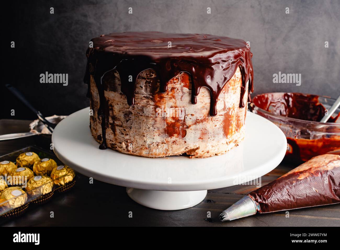 Schokoladenkuchen mit Haselnussfrosting bedeckt mit Schokoladenganache: Kuchen auf einem Kuchenständer mit dunkler Schokoladenglasur, die an den Seiten tropft Stockfoto