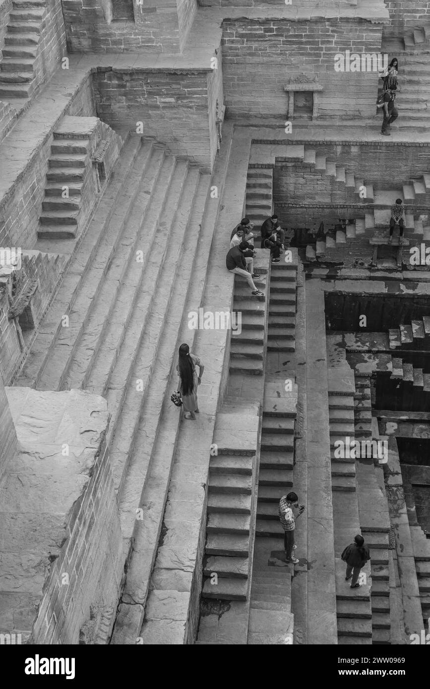Jodhpur, Rajasthan, Indien - 17. Dezember 2023: Menschen sitzen auf der architektonischen antiken Treppe Toorji Ka Jhalra Bavdi, schwarz weiß Stockfoto