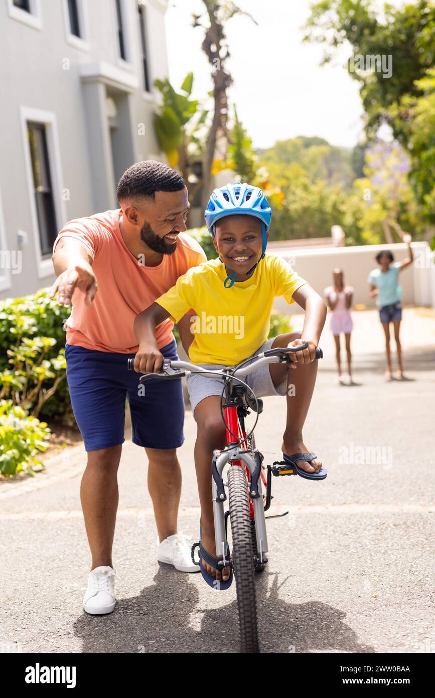 Ein junger afroamerikanischer Vater bringt seinem Sohn bei, draußen Fahrrad zu fahren Stockfoto