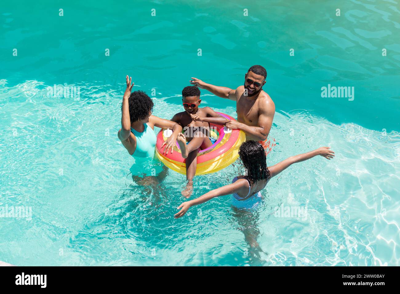 Eine afroamerikanische Familie genießt einen sonnigen Tag im Pool, türkisfarbenes Wasser glitzert Stockfoto