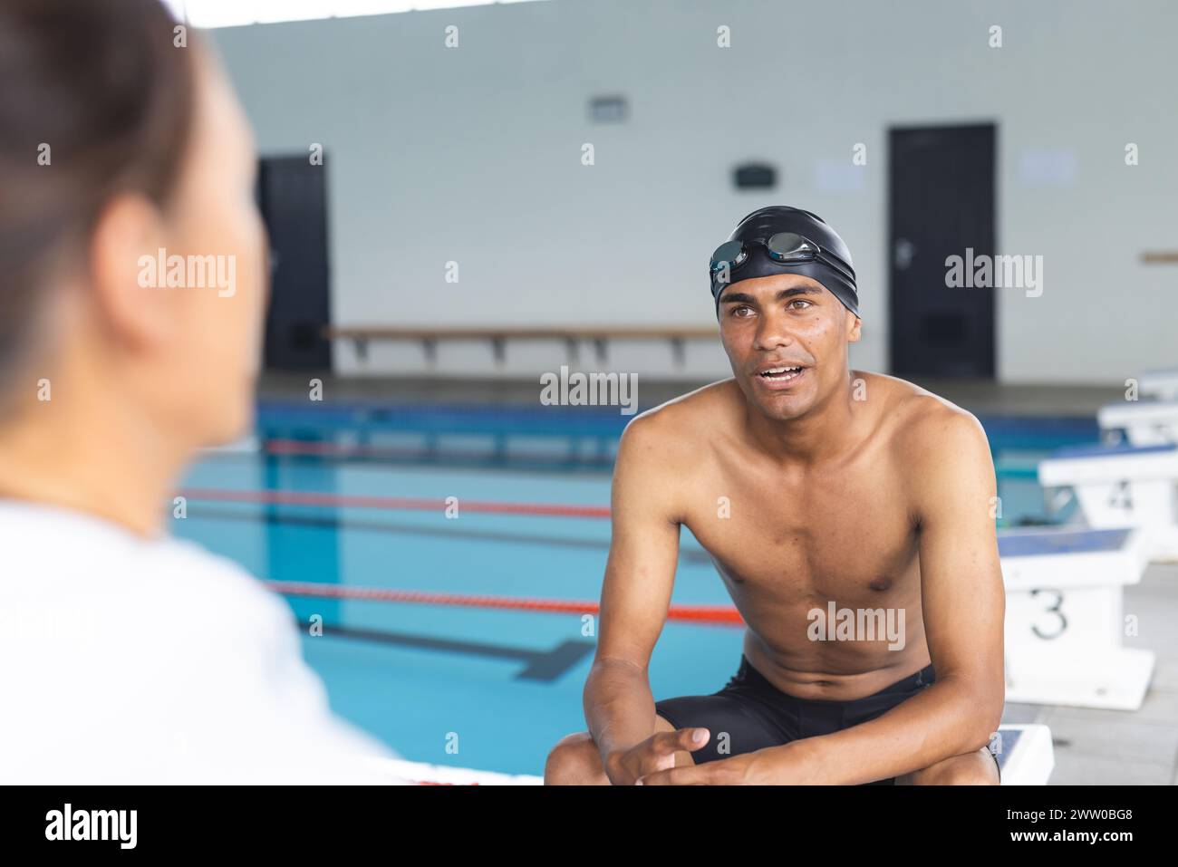 Ein fitter, hispanischer Sportler mittleren Alters unterhält sich mit einer Frau am Pool Stockfoto
