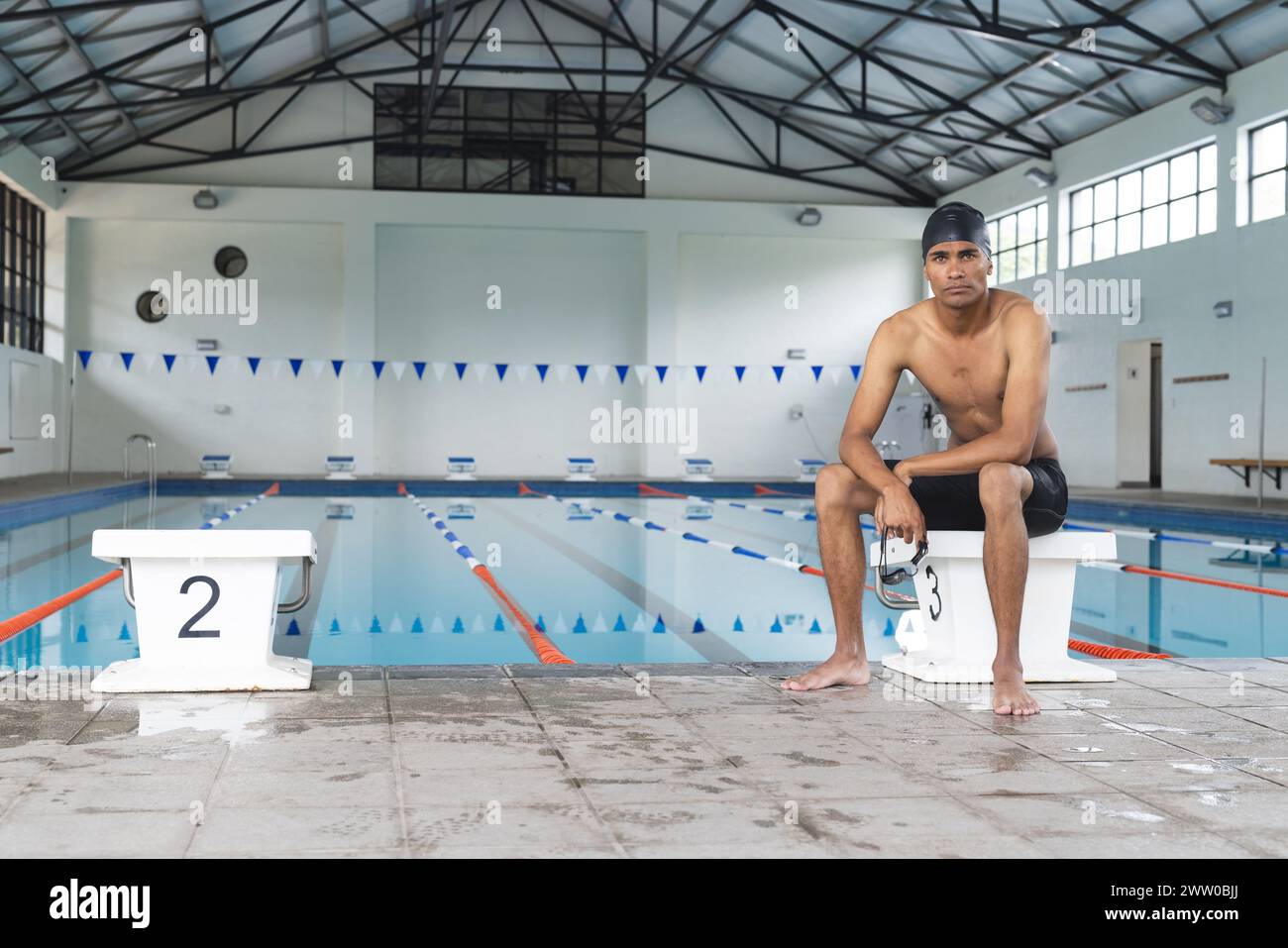 Ein junger afroamerikanischer Sportlerschwimmer sitzt am Pool, mit fokussiertem Blick und Kopierraum Stockfoto