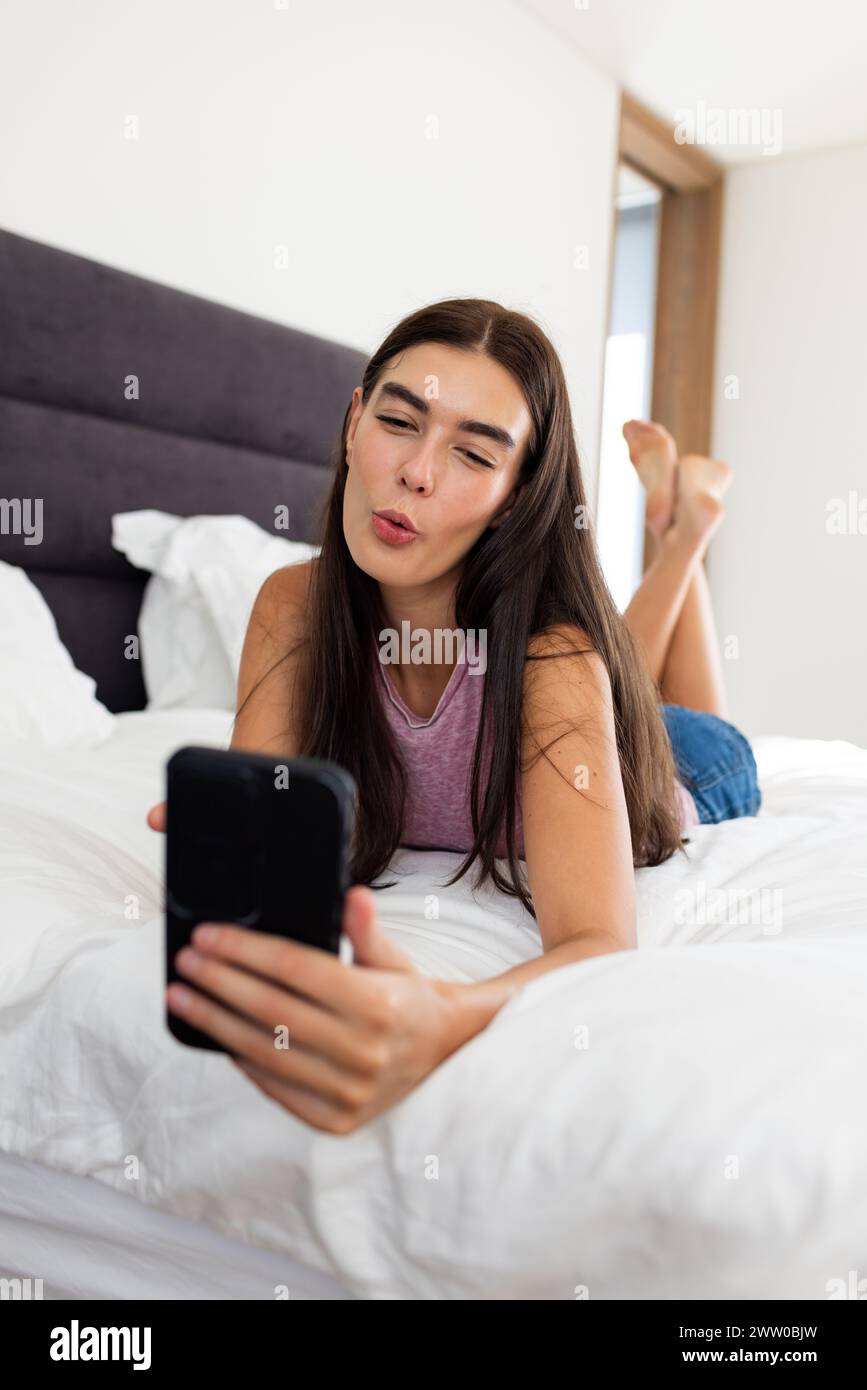 Eine junge weiße Brünette macht zu Hause ein Selfie auf ihrem Bett Stockfoto